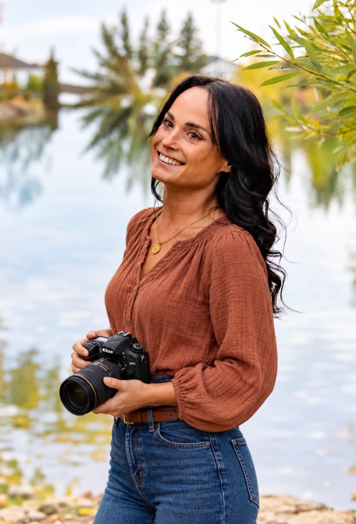 Ckenzie Hatton, St. Albert boudoir photographer, smiling with her camera by the water